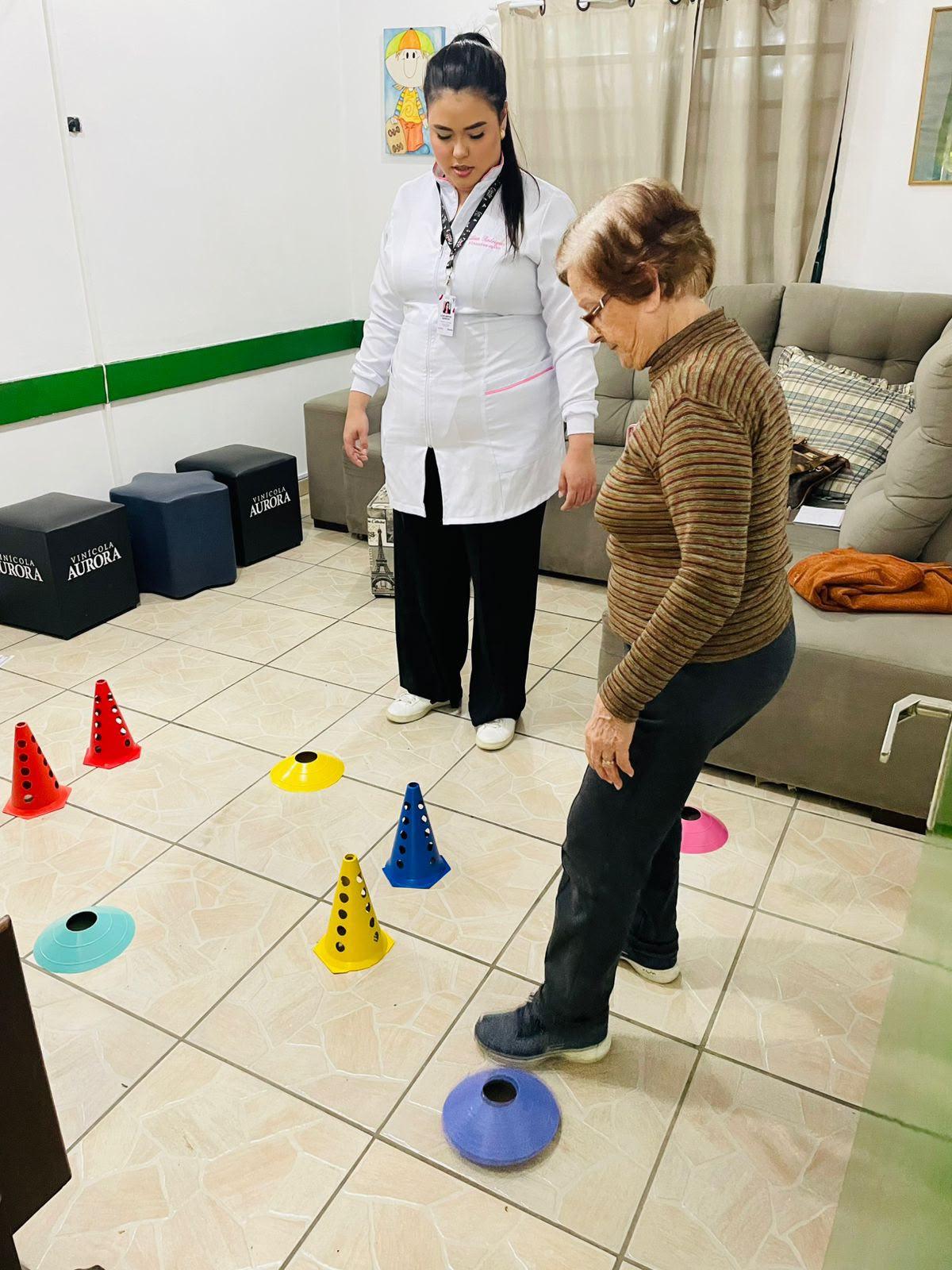 Estagiária acompanha uma idosa em exercício de equilíbrio entre cones coloridos