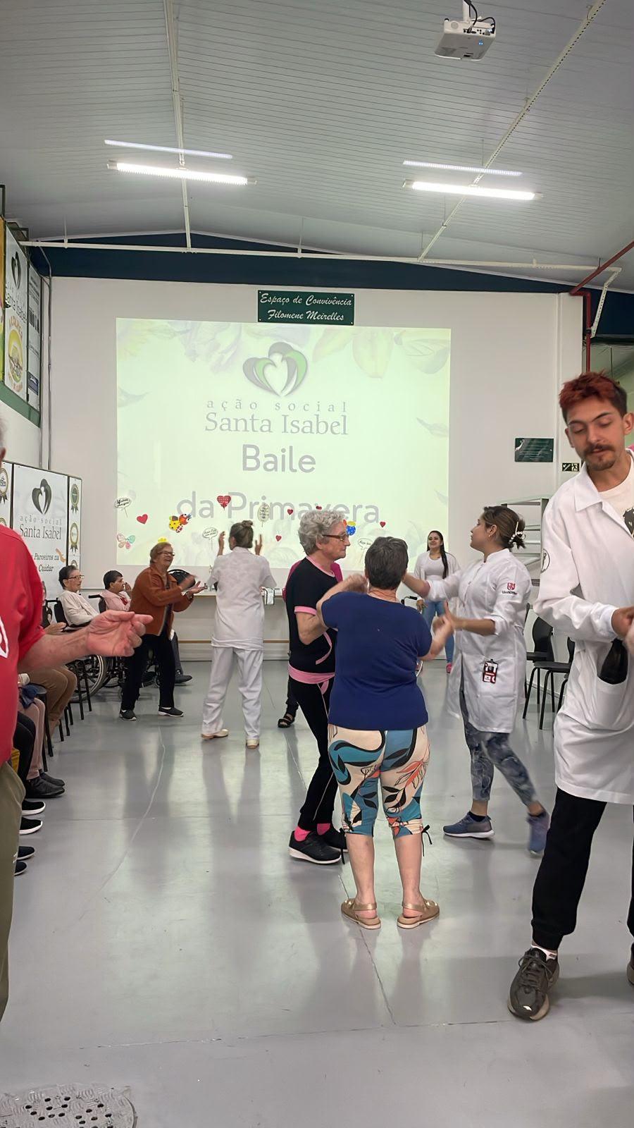 Estagiários e idosos dançam no salão durante o Baile de Primavera