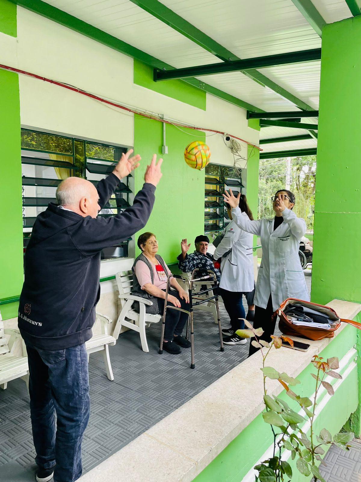 Idoso e estagiária erguem os braços em exercício na varanda da casa